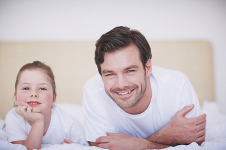 Enjoying a lazy morning together...A father and daughter lying side by side on a bed.の写真素材