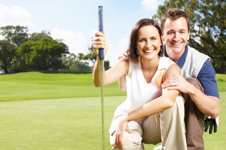 They enjoy golfing together as a hobby. Young couple smiling and crouched together on the golf course.の写真素材