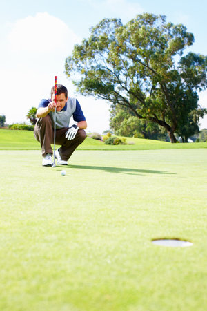Male golfer lining up the putt. Full length of crouched male golfer on the putting green lining up the putt.の写真素材