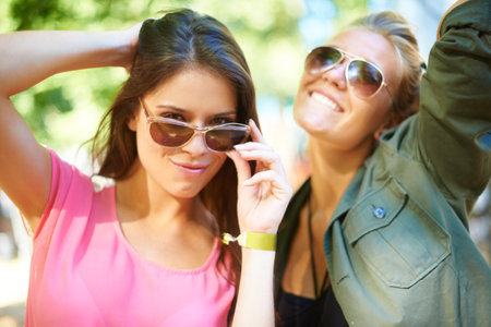 Care-free style. Two young woman standing outside wearing sunglasses.の写真素材