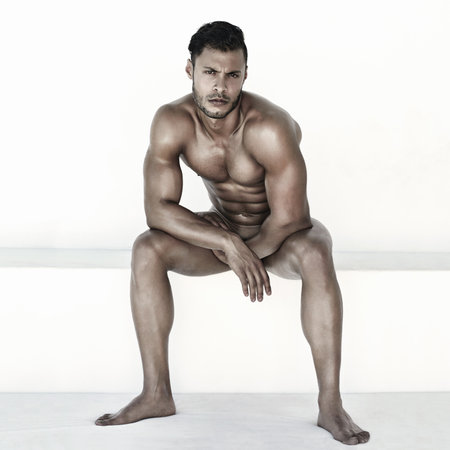 Nude, body and man in portrait isolated on a wall background for health, fitness and wellness. Naked, strong and face of a sexy male model sitting with muscles for power, sports and exercise resultsの写真素材