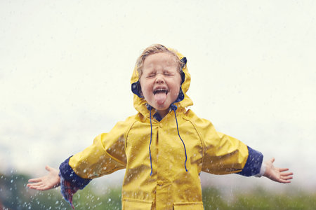 Winter, raincoat and a girl playing in the rain outdoor alone, having fun during the cold season....