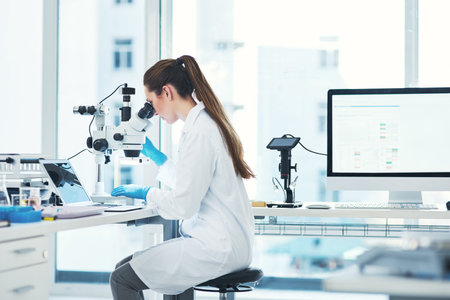 This is a delicate process. a focused young female scientist looking through a microscope while...