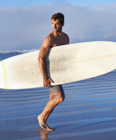 Chasing waves is his passion. A handsome young surfer at the beach craving a good wave.の写真素材