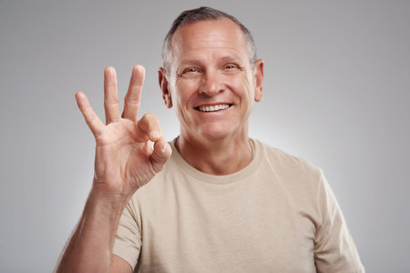 Everything is a-okay. a handsome mature man standing against a grey background in the studio and...