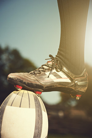 Conquering the world of rugby. a rugby players foot resting on the match ball.の写真素材