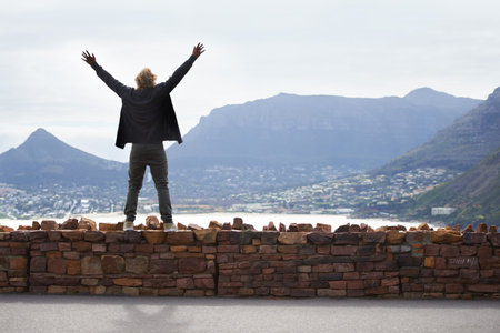 Feeling on top of the world. a young man standing on a wall with his arms open looking at the...