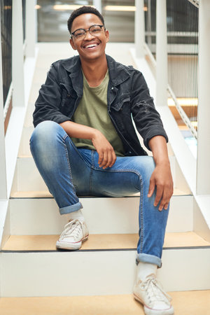Im here for success every step of the way. Portrait of a confident young businessman sitting on the steps of a modern office.の写真素材