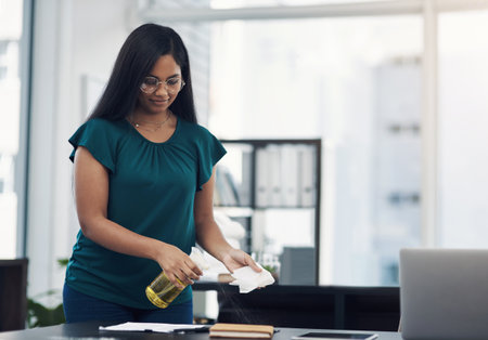 A clean desk can reduce the potential spread of germs. a young businesswoman cleaning a workspace in an office.の写真素材