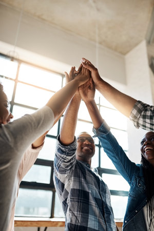 Work together and youre already winning. a group of creatives high-fiving in an office.の写真素材