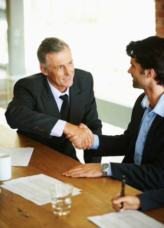 Im looking forward to doing business with you. Two businessmen seated at a table and shaking hands.の写真素材