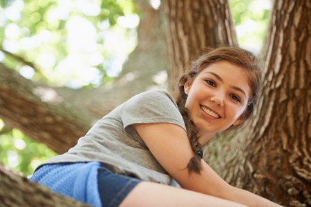 Catch me if you can. Portrait of a teenage girl sitting high up in a tree.の写真素材