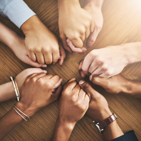Drawing strength and support from each other. Closeup shot of a group of businesspeople sitting together at a table and holding hands.の写真素材