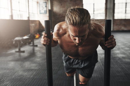 It takes power and perseverance. a muscular young man pushing a weight sled in a gym.