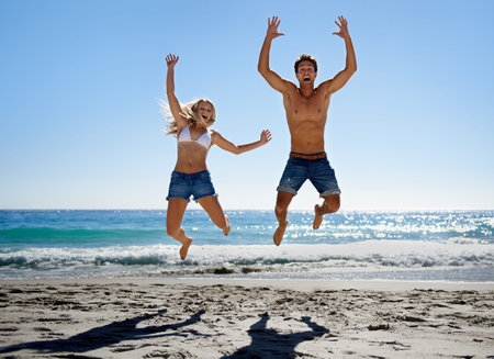 Jumping in the sun. A young couple jumping into the air while enjoying a day on the beach.
