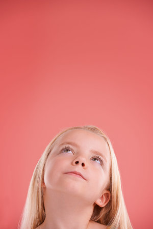 That looks intresting. Studio shot of a young girl posing on an orange background.の写真素材