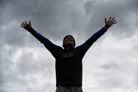 Triumphant ascent. A young man celebrating at the top of a mountain after reaching the summit.