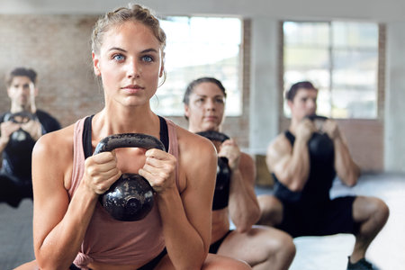 Fitness, kettlebell and personal trainer doing a workout with a group for strength training in a...