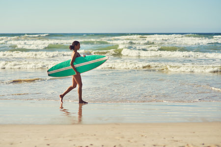 Its time to hit the waves. a young woman out at the beach with her surfboard.の写真素材