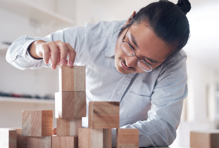 Innovation is the catalyst for change. a young businessman working with wooden building blocks in a...