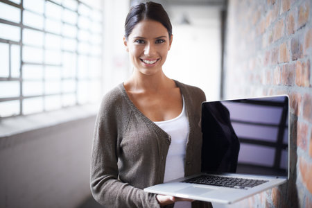 I couldnt do business without it. Attractive young woman holding up a laptop with a smile.の写真素材