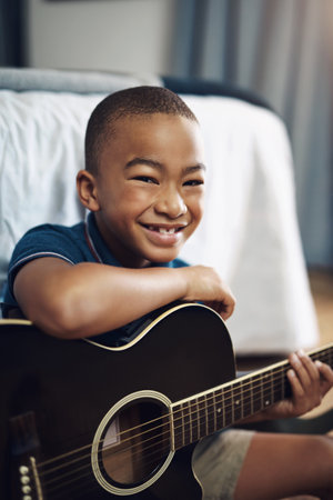 This is my first instrument. a young boy playing the guitar at home.の写真素材