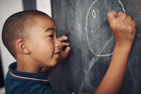 Drawing has numerous developmental benefits. a young boy writing on a blackboard at home.の写真素材