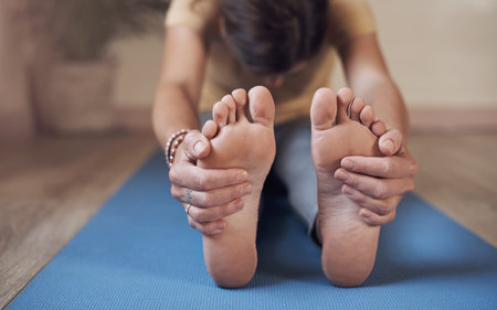 Feel the stretch. an unrecognizable woman sitting alone and stretching while holding her feet in a yoga studio.の写真素材