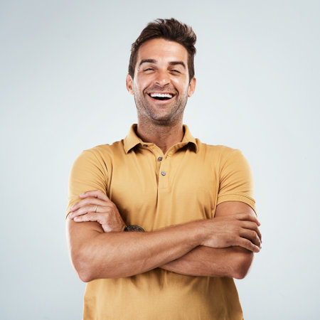 Im listening to you. Portrait of a cheerful young man smiling brightly with his arms folded while standing against a grey background.の写真素材