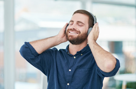 When you feel good, you do good. a happy young businessman using headphones in a modern office.の写真素材