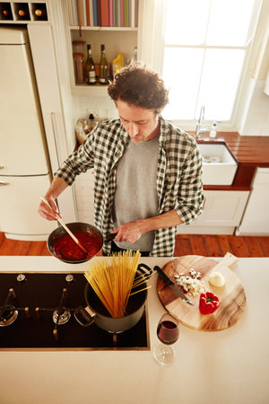 Spaghetti, cooking or above of man in kitchen with healthy vegan diet for nutrition or vegetables at home in Australia. Wine glass, food or male person in house kitchen in preparation for dinner mealの写真素材