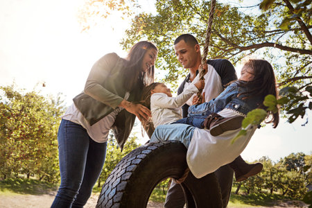 Making sure their earliest memories will be good ones. a happy mother and father pushing their daughters on a tyre swing.