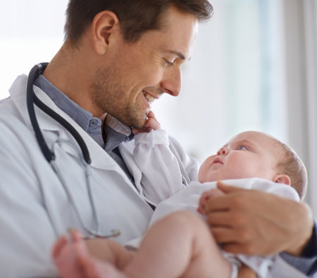Happy male doctor, pediatrician and holding baby for hospital assessment, medical support and growth. Pediatrics, physician and carrying newborn kid in clinic, healthcare service and helping childrenの写真素材