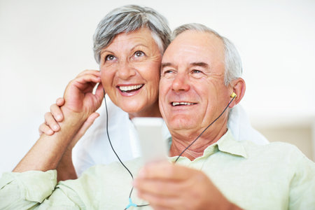 Smiling mature man and woman listening music. Smiling mature man and woman listening music while relaxing at home.の写真素材