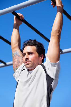 Man, fitness and pull ups on monkey bars in park gym for weightlifting, exercise or workout in nature. Fit, active and strong male lifting body weight or hanging on iron bar for strength exercisingの写真素材