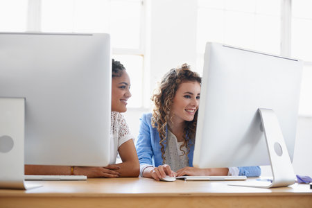 Women, computer or happy people in office talking, chatting or speaking of gossip or online news together. Internet, smile or friends in conversation or discussion about on blog or article at deskの写真素材