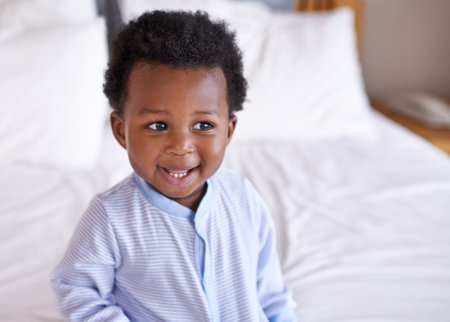 Happy, curious and baby laughing in bed, waking up and playing in his home. Face, smile and african boy toddler in a bedroom cheerful, having fun and sweet, cute and playful while relaxing aloneの写真素材