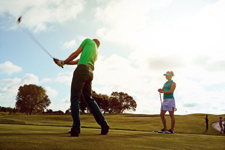 Every swing makes him a better player. a couple playing golf together on a fairway.