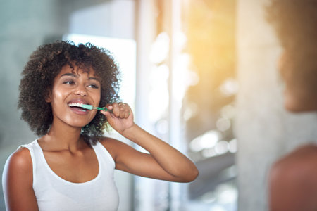 Mirror, dental and black woman brushing teeth, fresh breath and oral health in the bathroom. Female person, happy model and lady with wellness, mirror and hygiene with morning routine and tooth careの写真素材