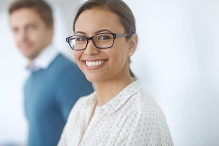 Our companys success starts with its staff. Portrait of an attractive young woman standing in an office with a coworker in the background.の写真素材