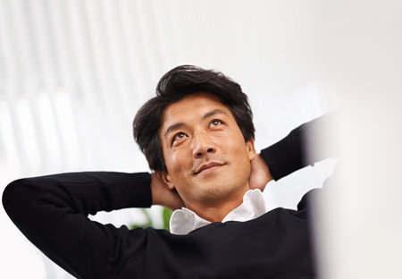 Thinking about business. A relaxed businessman sitting with his hands behind his head at his desk.の写真素材