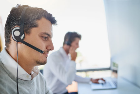 Were on standby to take your calls. a young call centre agent working in an office with his...