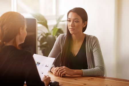 Interview, discussion and business women in office in conversation, talking and planning at desk. Communication, partnership and female workers with document for recruitment, hiring and collaborationの写真素材