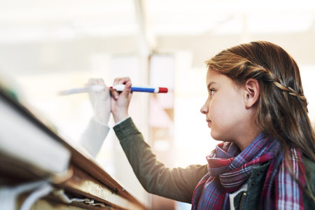 Shes teaching the whole class a lesson today. an elementary school girl writing on a whiteboard in class.の写真素材