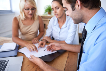 This team is taking the company to the top. Three young executives sitting around a table discussing paperwork.の写真素材