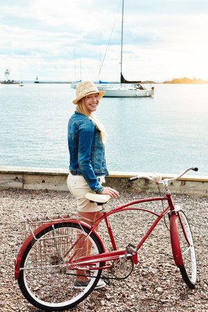 Couldnt have asked for a better day to go riding my bike. Portrait of a cheerful young woman getting ready to ride her bicycle while looking at the camera outside during the day.の写真素材