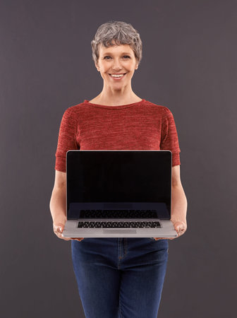 Introducing my new website. Studio portrait of an elderly woman holding a laptop against a gray...