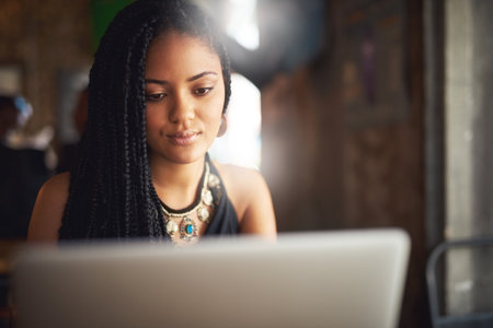 Adding some new content to her blog. an attractive young woman using her laptop in a coffee shop.の写真素材
