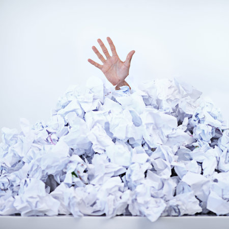 Buried under his work. a businessman buried under a pile of crumpled up paperwork.