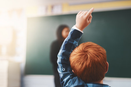 Hand, student and child in classroom with question for teacher, education and learning with school blackboard. Boy, raise arm and questions for knowledge, information and development in classの写真素材